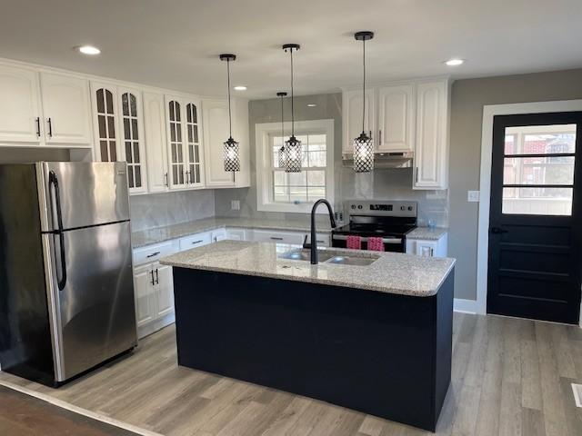 kitchen featuring appliances with stainless steel finishes, sink, white cabinets, a kitchen island with sink, and light stone countertops