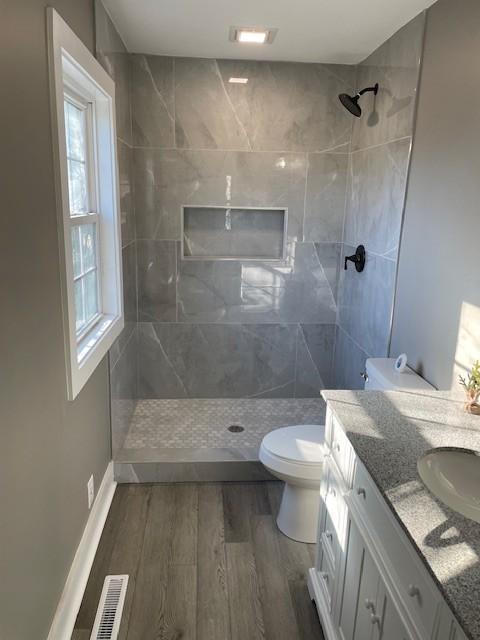 bathroom featuring hardwood / wood-style flooring, vanity, a tile shower, and toilet