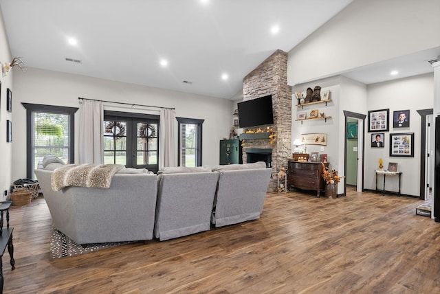 living room featuring a wealth of natural light, a stone fireplace, wood-type flooring, and high vaulted ceiling