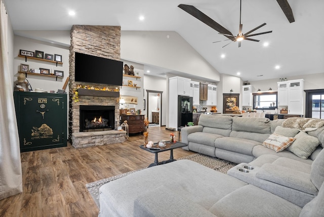 living room with ceiling fan, a stone fireplace, wood-type flooring, and high vaulted ceiling