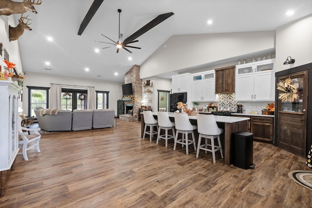 kitchen featuring a center island, black refrigerator with ice dispenser, high vaulted ceiling, a stone fireplace, and a breakfast bar area