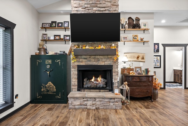 living room with a stone fireplace, lofted ceiling, and wood-type flooring