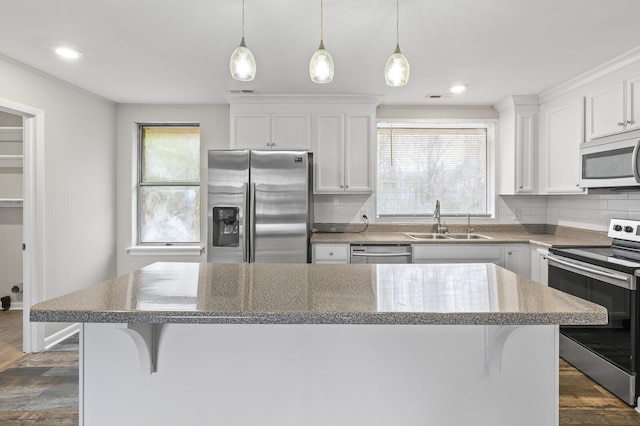 kitchen with appliances with stainless steel finishes, backsplash, sink, white cabinets, and a center island