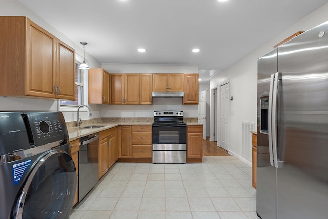 kitchen with appliances with stainless steel finishes, light stone counters, sink, washer / dryer, and hanging light fixtures