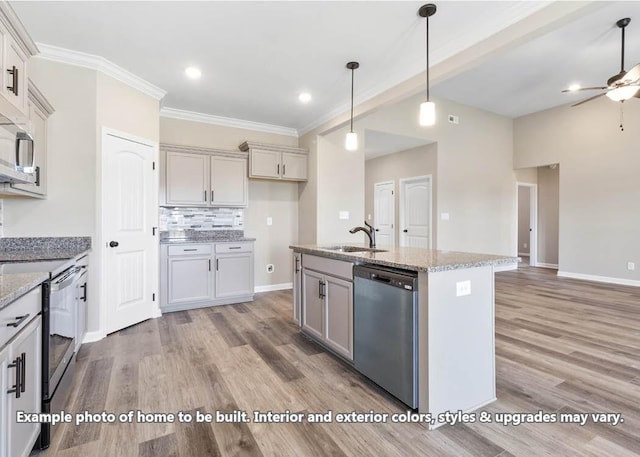 kitchen with hanging light fixtures, sink, an island with sink, appliances with stainless steel finishes, and light stone counters