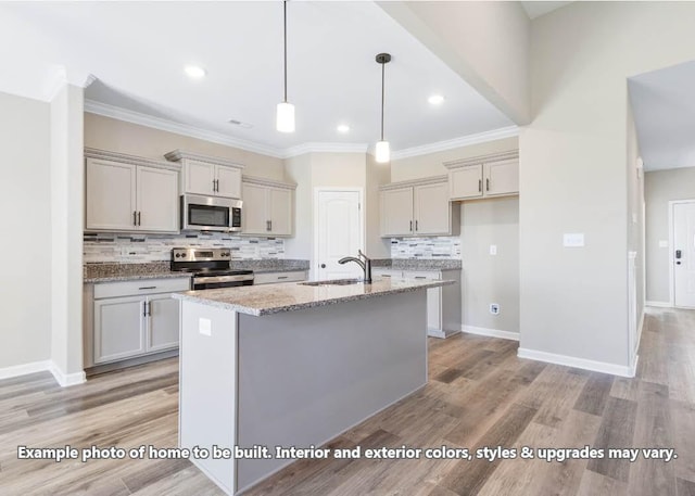 kitchen featuring pendant lighting, a center island with sink, sink, appliances with stainless steel finishes, and light stone counters