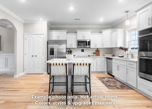 kitchen with crown molding, white cabinetry, hanging light fixtures, stainless steel appliances, and light hardwood / wood-style floors