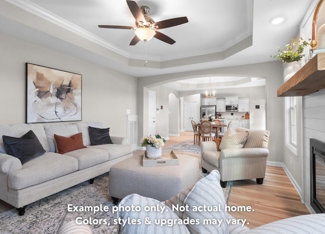 living room featuring crown molding, ceiling fan, a tray ceiling, and light wood-type flooring