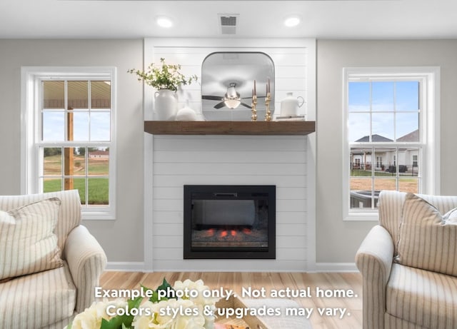 living room featuring a healthy amount of sunlight, a large fireplace, and light hardwood / wood-style floors