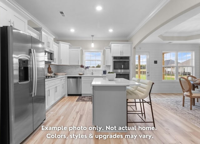 kitchen with a breakfast bar, white cabinetry, appliances with stainless steel finishes, pendant lighting, and light hardwood / wood-style floors