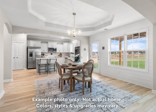 dining room with ornamental molding, a healthy amount of sunlight, a tray ceiling, and light hardwood / wood-style flooring