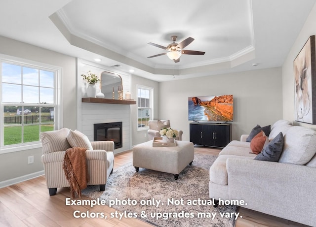 living room with a large fireplace, wood-type flooring, a tray ceiling, and a wealth of natural light