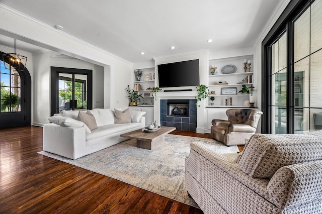 living room featuring hardwood / wood-style flooring, built in shelves, ornamental molding, and a chandelier