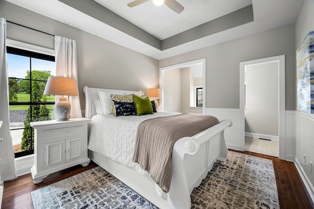 bedroom with ceiling fan, dark hardwood / wood-style flooring, a raised ceiling, and multiple windows