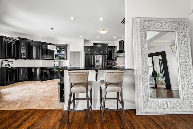 kitchen featuring hanging light fixtures, wall chimney range hood, stainless steel fridge with ice dispenser, a kitchen bar, and decorative backsplash