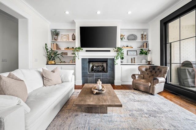 living room featuring hardwood / wood-style flooring, built in shelves, ornamental molding, and a tile fireplace