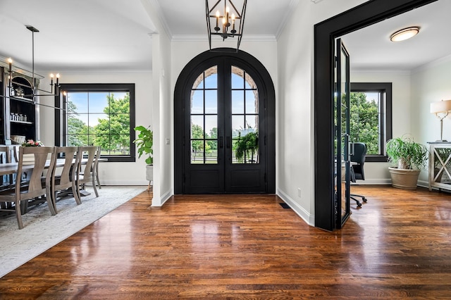 foyer featuring crown molding, french doors, dark wood-type flooring, and a notable chandelier