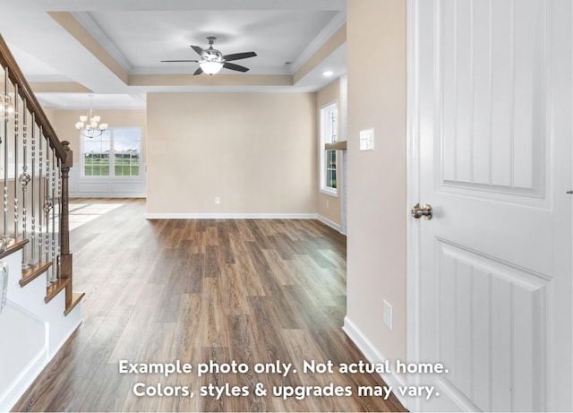 unfurnished living room featuring dark wood-type flooring, ornamental molding, a tray ceiling, and ceiling fan with notable chandelier