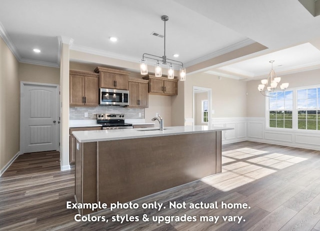 kitchen with ornamental molding, appliances with stainless steel finishes, a kitchen island with sink, and sink