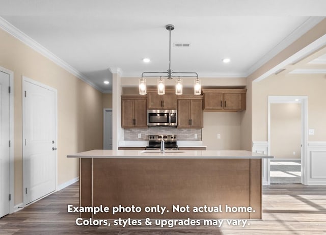 kitchen featuring sink, crown molding, hardwood / wood-style floors, hanging light fixtures, and a center island with sink