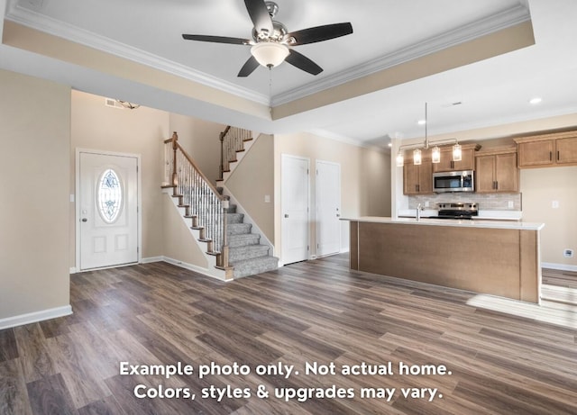 kitchen featuring ornamental molding, appliances with stainless steel finishes, a raised ceiling, an island with sink, and pendant lighting