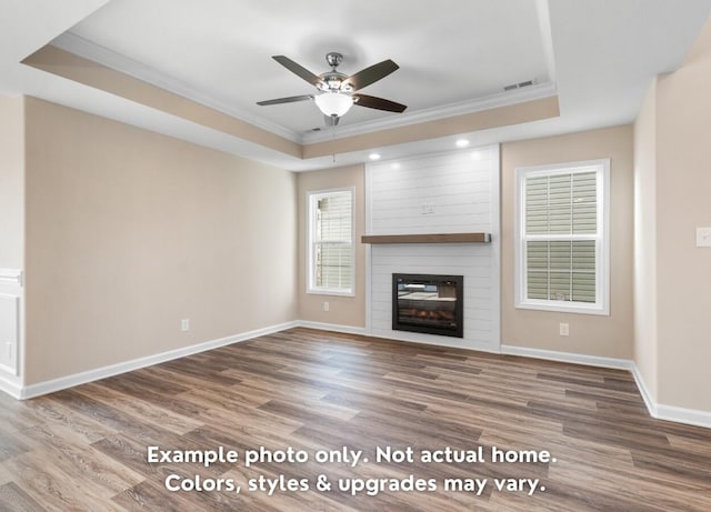 unfurnished living room with crown molding, a large fireplace, wood-type flooring, and a raised ceiling