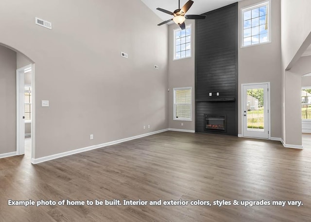 unfurnished living room with dark hardwood / wood-style flooring, a towering ceiling, a large fireplace, and ceiling fan