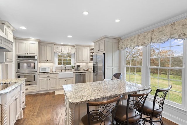 kitchen with sink, a center island, light stone counters, dark hardwood / wood-style floors, and appliances with stainless steel finishes