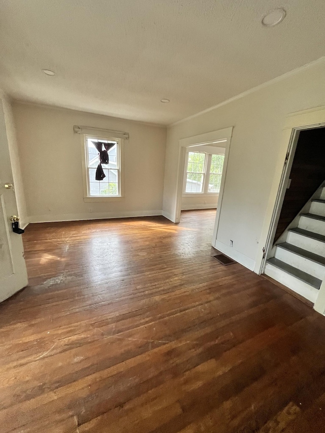 unfurnished room featuring wood finished floors, visible vents, baseboards, and stairs