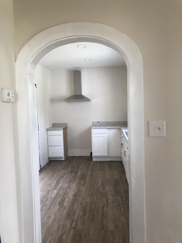 interior space featuring arched walkways, dark wood-style flooring, light countertops, white cabinets, and wall chimney range hood