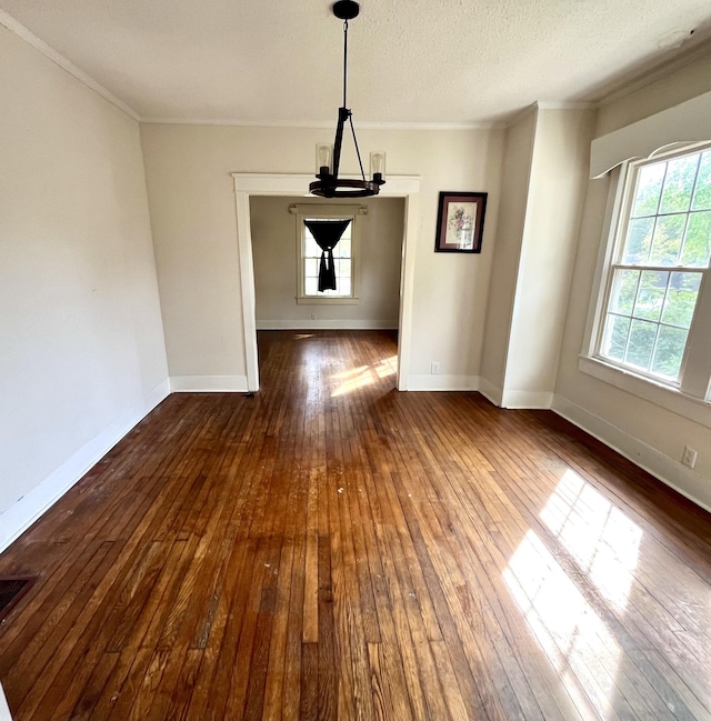 unfurnished dining area featuring baseboards, a textured ceiling, ornamental molding, and wood finished floors