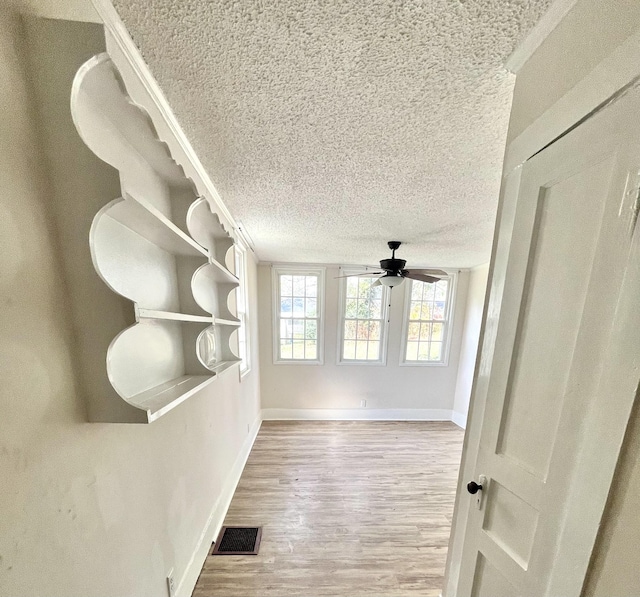 interior space featuring baseboards, visible vents, light wood-style flooring, ceiling fan, and a textured ceiling