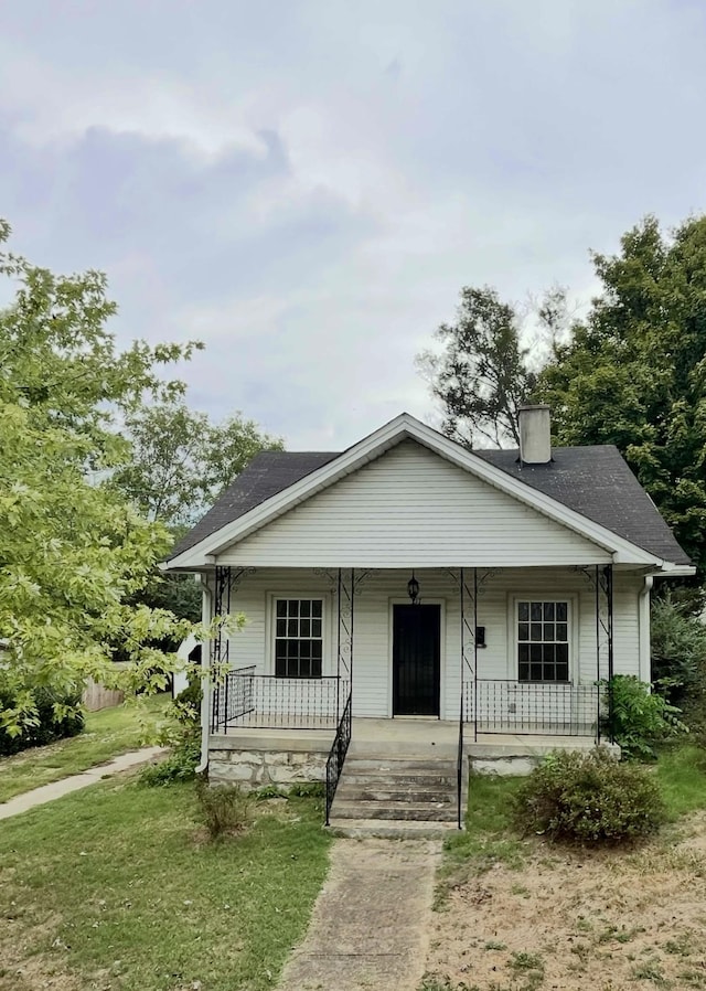 bungalow-style house with a shingled roof, covered porch, and a chimney