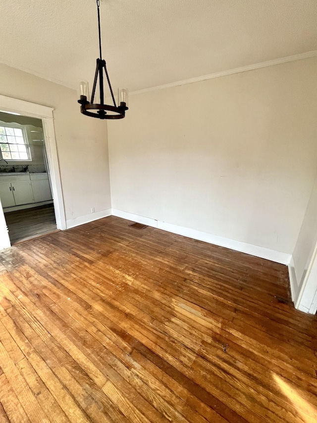 unfurnished dining area featuring baseboards, crown molding, a chandelier, and wood finished floors