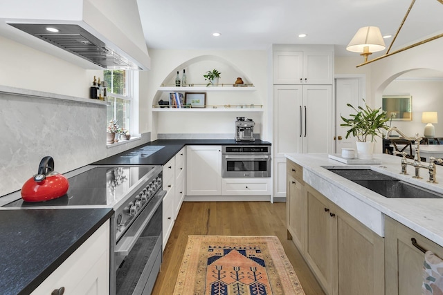 kitchen with white cabinets, wall chimney range hood, sink, appliances with stainless steel finishes, and light hardwood / wood-style floors