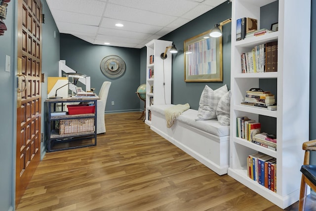 sitting room featuring built in shelves, a paneled ceiling, and hardwood / wood-style flooring