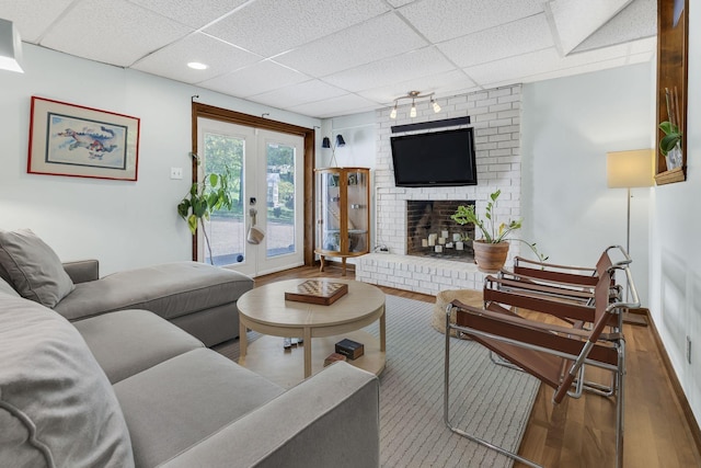 living room featuring a paneled ceiling, french doors, wood-type flooring, and a brick fireplace