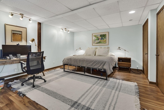 bedroom featuring a drop ceiling, wood-type flooring, and track lighting