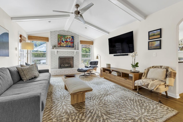 living room featuring vaulted ceiling with beams, ceiling fan, hardwood / wood-style floors, and a brick fireplace