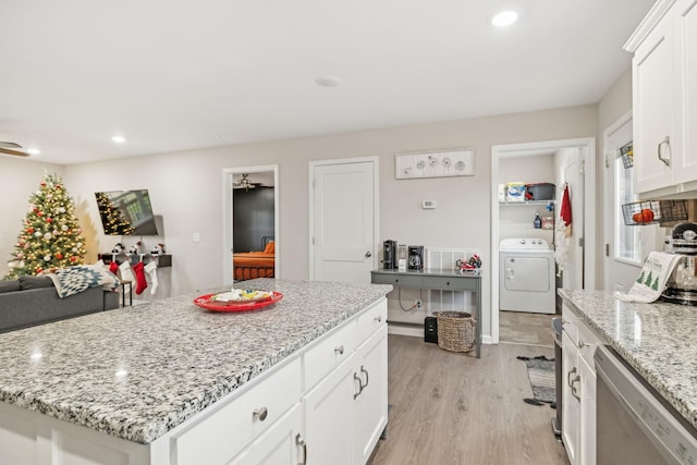 kitchen with light stone countertops, a kitchen island, stainless steel dishwasher, washer / clothes dryer, and white cabinets