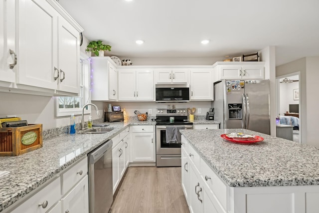 kitchen featuring appliances with stainless steel finishes, light wood-type flooring, light stone counters, sink, and white cabinets