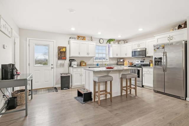 kitchen featuring a kitchen breakfast bar, white cabinets, light stone counters, a kitchen island, and appliances with stainless steel finishes