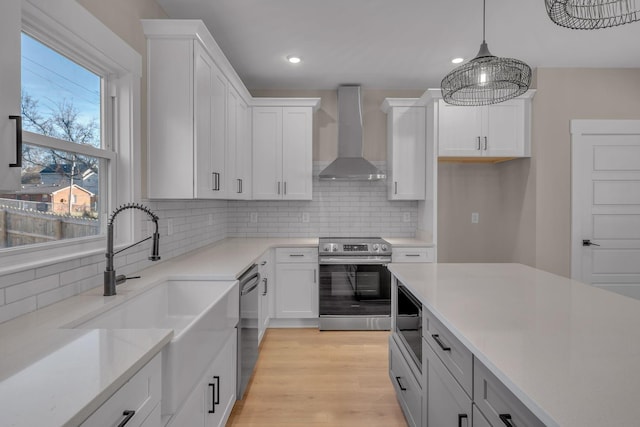 kitchen with backsplash, white cabinets, hanging light fixtures, wall chimney exhaust hood, and appliances with stainless steel finishes