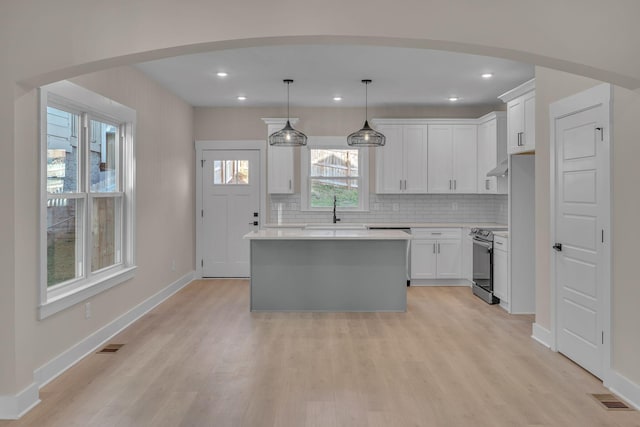 kitchen with a center island, hanging light fixtures, stainless steel electric range oven, tasteful backsplash, and white cabinetry