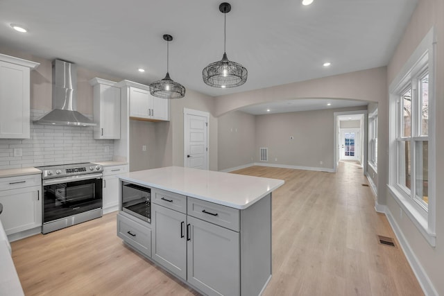 kitchen with stainless steel range with electric stovetop, built in microwave, wall chimney range hood, a kitchen island, and hanging light fixtures