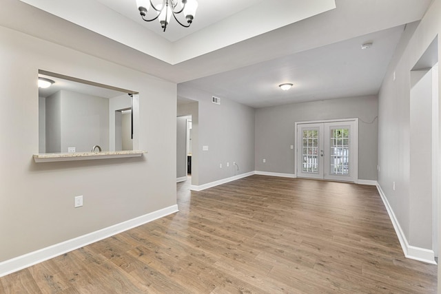 empty room with hardwood / wood-style floors, french doors, and an inviting chandelier