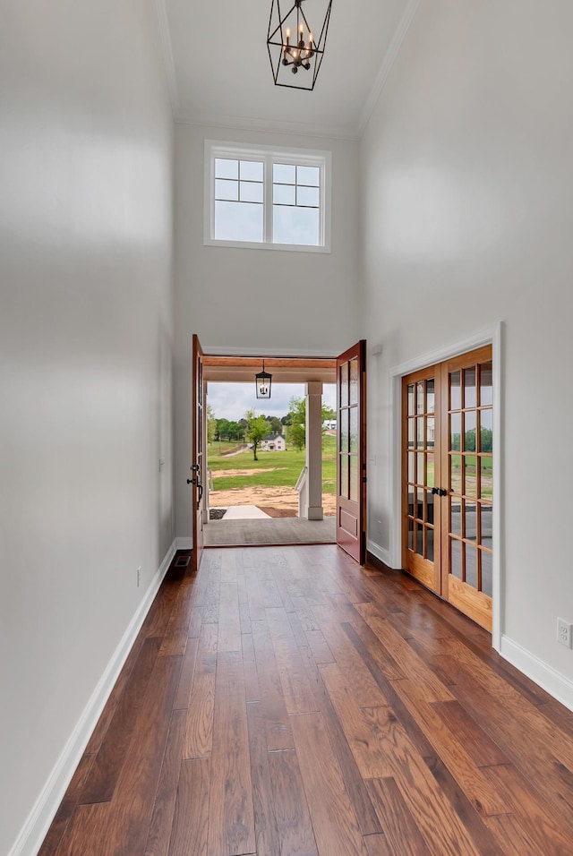 entrance foyer with a high ceiling, french doors, dark hardwood / wood-style floors, a chandelier, and crown molding