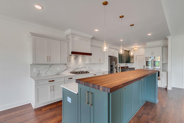 kitchen featuring white cabinetry, butcher block counters, a center island with sink, appliances with stainless steel finishes, and pendant lighting