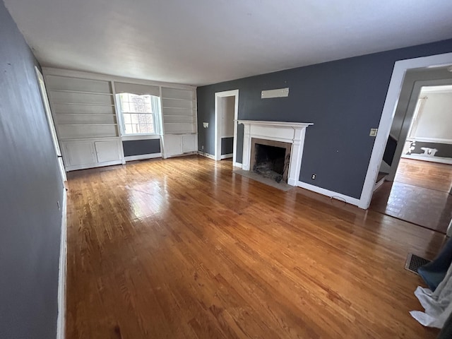 unfurnished living room featuring built in shelves and wood-type flooring