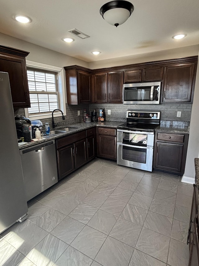 kitchen with sink, stainless steel appliances, dark stone countertops, decorative backsplash, and dark brown cabinetry